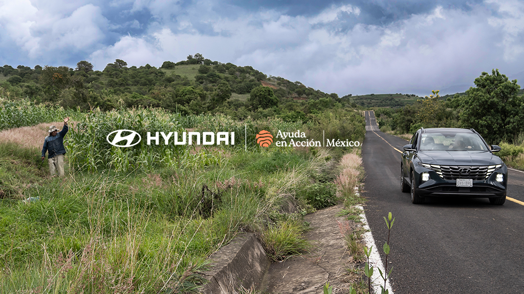 Persona en un pastizal junto a la carretera saludando a un conductor en una Hyundai Tucson